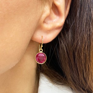 Peut inclure: Boucles d'oreilles en or avec une pierre précieuse ronde rouge. Les boucles d'oreilles sont pendantes et ont un design simple.