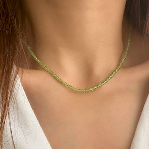 Può includere: Una delicata collana di perline verdi con piccole perline di forma quadrata. La collana è indossata da una persona, ma l'attenzione è rivolta alla collana stessa.