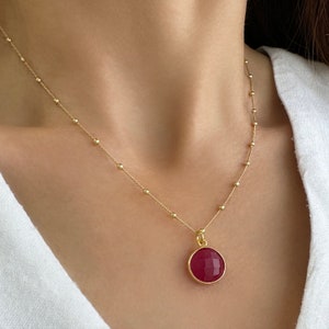 Op de afbeelding: Een gouden ketting met een ronde hanger van rode edelsteen.