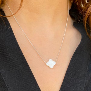 Puede incluir: Un collar de cadena de plata con un colgante de trébol de cuatro hojas blanco texturizado.