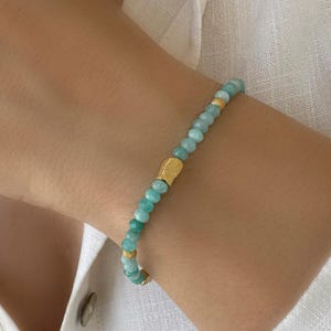 Peut inclure: Un bracelet composé de petites perles de pierre gemme bleu-vert à facettes disposées en un brin continu. Le design est rehaussé par trois intercalaires en métal doré, dont une pièce centrale texturée et deux perles rondes plus petites.