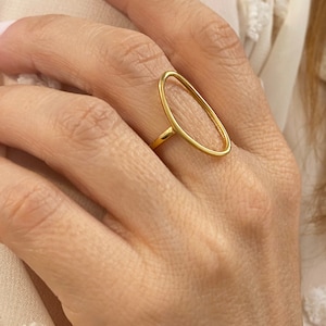 May include: A gold oval ring with a simple, minimalist design. The ring is open and has a smooth, polished finish.