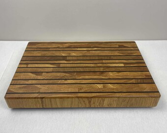 May include: A rectangular wooden cutting board with a light brown color and dark brown lines. The cutting board is made of multiple wood pieces and has a smooth surface. The board is designed for kitchen use.