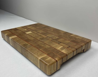 May include: A rectangular wooden cutting board with a butcher block design. The board is made of various wood pieces, creating a mosaic pattern of light and dark brown tones. It has rounded edges and a smooth finish.