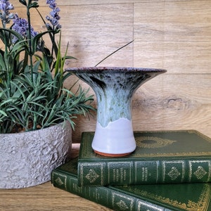 May include: A ceramic vase with a wide, flared opening and a green and white glaze. The vase is sitting on top of a stack of books with gold lettering.