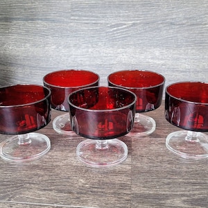 May include: Set of five clear glass dessert dishes with a red base. The dishes have a short stem and a round bowl.