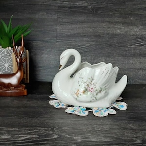May include: White porcelain swan planter featuring a floral design. The swan has a delicate, graceful shape and is ideal for displaying small plants or flowers.