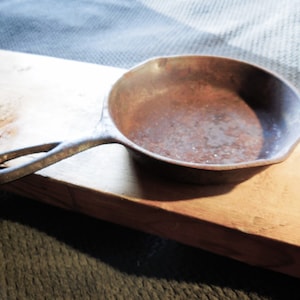 May include: A small, rusty cast iron skillet with a short handle. The skillet is sitting on a wooden surface.