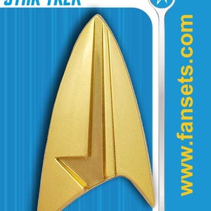 May include: A gold Star Trek insignia pin on a blue background with the text "STAR TREK" and "www.fansets.com".