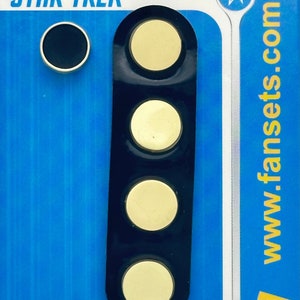 May include: A blue Star Trek collectible card featuring a black and gold pin set. The set includes a small black pin and a strip of four gold pins. The packaging includes the Star Trek logo and the website www.fansets.com.