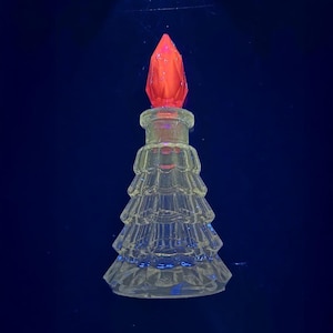 Könnte beinhalten: Eine klare Glasparfümflasche mit einem Weihnachtsbaumdesign. Die Flasche hat einen roten, facettierten Verschluss. Die Flasche ist etwa 13 cm hoch.