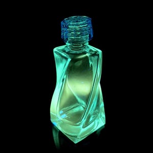 May include: A clear glass perfume bottle with a teal tint and a blue screw-on cap. The bottle has a unique, twisted design and is illuminated, creating a glowing effect against a black background. The bottle is empty.