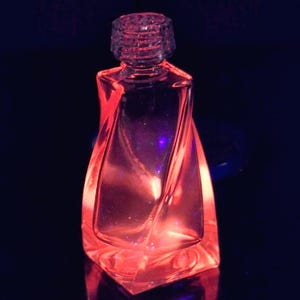 May include: A clear glass bottle with a twisted design, illuminated with a red glow. The bottle has a square base and a textured, cylindrical stopper. The background is dark, emphasizing the bottle's shape and color.