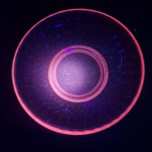 Könnte beinhalten: Ein kreisförmiges Objekt mit einem rosa Außenrand und einem rosa Innenkreis. Die Mitte ist ein helleres Rosa. Der Hintergrund ist dunkelblau. Das Objekt scheint aus einem transparenten Material zu bestehen.