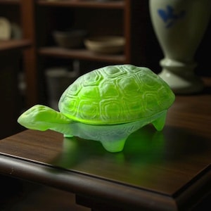 Pode incluir: Uma figura de tartaruga de vidro verde brilhante com uma carapaça texturizada e pernas visíveis. A tartaruga está sobre uma superfície de madeira escura. O objeto é decorativo.