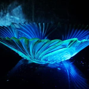 May include: A glowing blue glass bowl with a scalloped rim. The bowl has a textured surface and is illuminated with a bright blue light, creating a striking visual effect. The bowl is likely a decorative item.