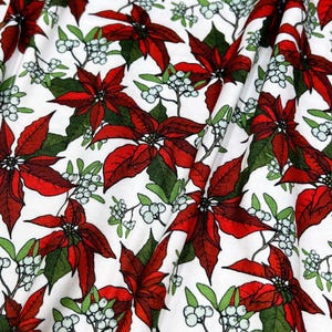 Puede incluir: Tela blanca con un patrón repetido de flores de pascua rojas, hojas verdes y pequeñas bayas blancas. La tela está doblada, creando sombras y profundidad. El diseño es festivo y adecuado para proyectos navideños.