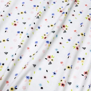 Puede incluir: Tela blanca con un pequeño estampado floral en tonos rosa, azul, amarillo y verde.