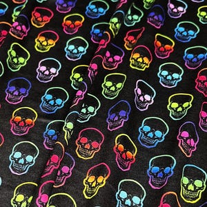 Puede incluir: Tela negra con un patrón repetido de calaveras coloridas. Cada calavera está delineada en un color neón vibrante, incluyendo rosa, amarillo, verde, azul y naranja. Las calaveras están espaciadas uniformemente en la tela.