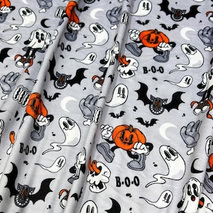 Puede incluir: Tela gris con temática de Halloween con un patrón repetido de fantasmas de dibujos animados, calabazas, murciélagos y manos. La tela también presenta el texto "B-0-0". Ideal para proyectos de manualidades.