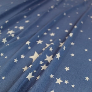 Puede incluir: Una tela azul con un patrón de estrellas blancas. La tela está arrugada y tiene un tacto suave y texturizado.