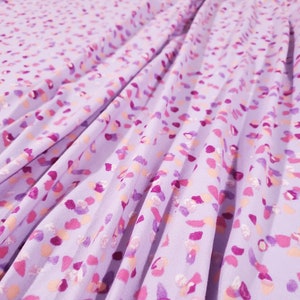 Puede incluir: Tela morada con un estampado abstracto blanco y rosa. La tela está plisada y tiene una textura suave y fluida.