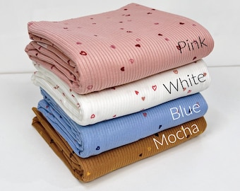 May include: Four different colors of ribbed fabric with a small heart print. The colors are pink, white, blue, and mocha. The fabric is folded and stacked on top of each other.