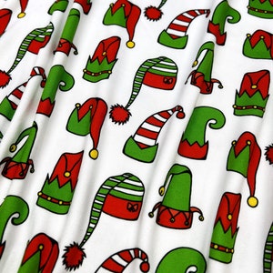 May include: White fabric with a repeating pattern of elf hats in red, green, and white. The hats are in various styles, including pointy, rounded, and with bells.
