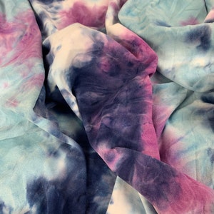 May include: A close-up of a tie-dye fabric in shades of blue, purple, and white. The fabric is soft and has a crinkled texture.