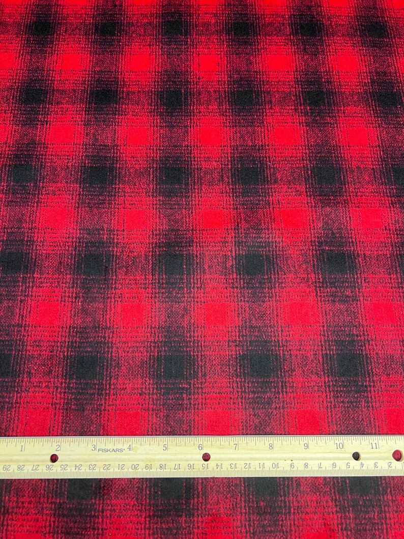 K&ouml;nnte beinhalten: Roter und schwarzer karierter Stoff mit leicht abgenutztem Look. Der Stoff wird mit einem Lineal in Zoll gemessen.