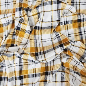 May include: A close-up of a white and yellow plaid fabric with black stripes. The fabric is wrinkled and has a textured surface.