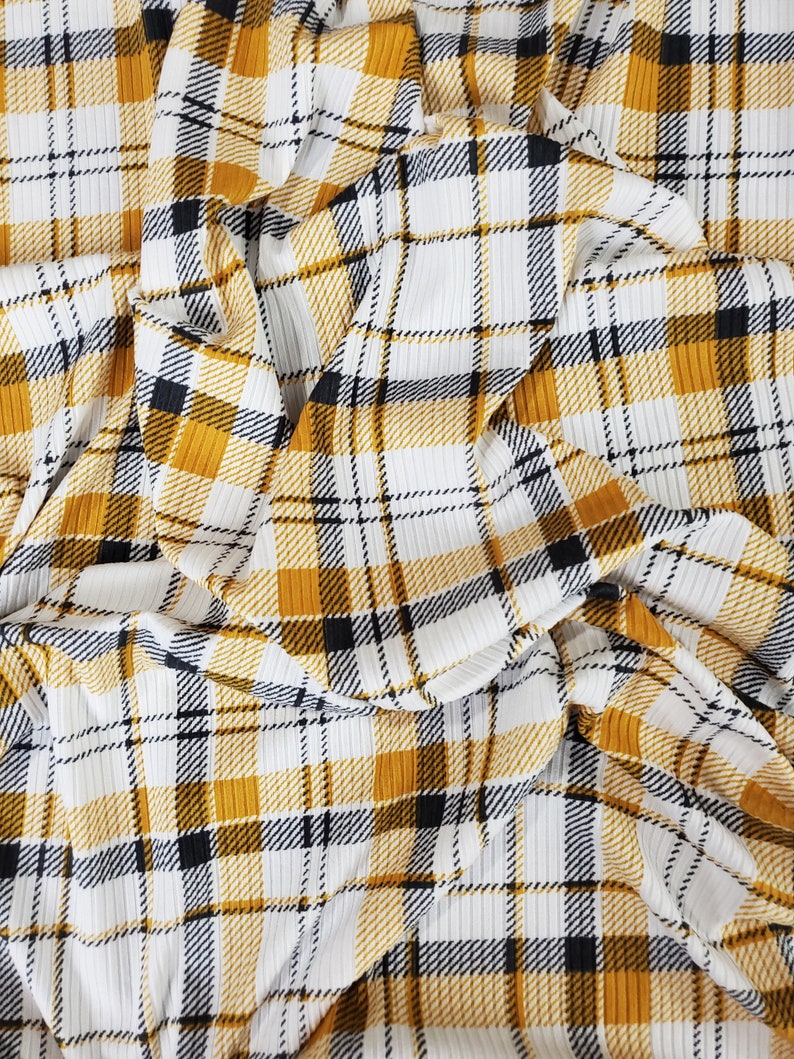 May include: A close-up of a white and yellow plaid fabric with black stripes. The fabric is wrinkled and has a textured surface.