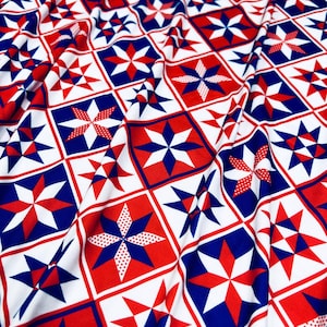 May include: Close-up of a fabric with a repeating pattern of red, white, and blue stars and geometric shapes. The design features a patchwork style with squares and starbursts, creating a patriotic or Americana theme.