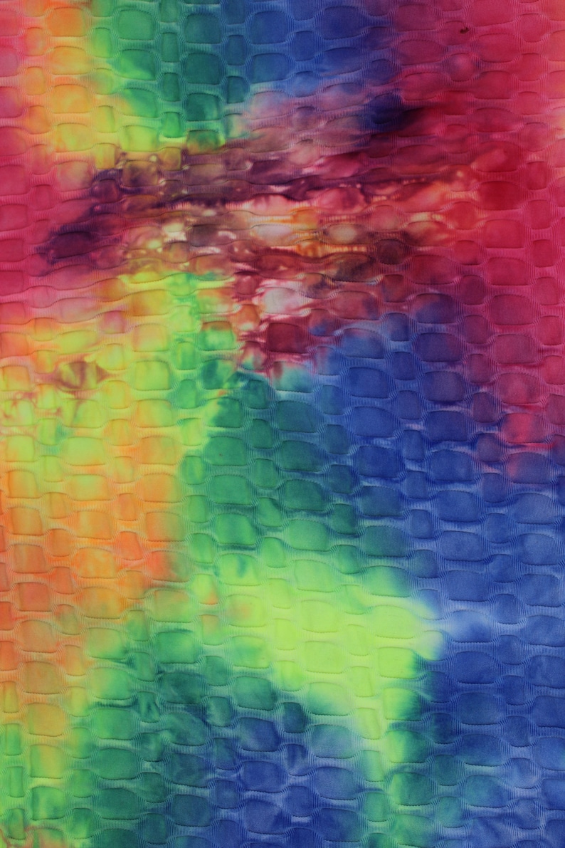 May include: A tie-dye fabric with a textured, embossed pattern. The fabric is a mix of blue, green, yellow, orange, and red colors.