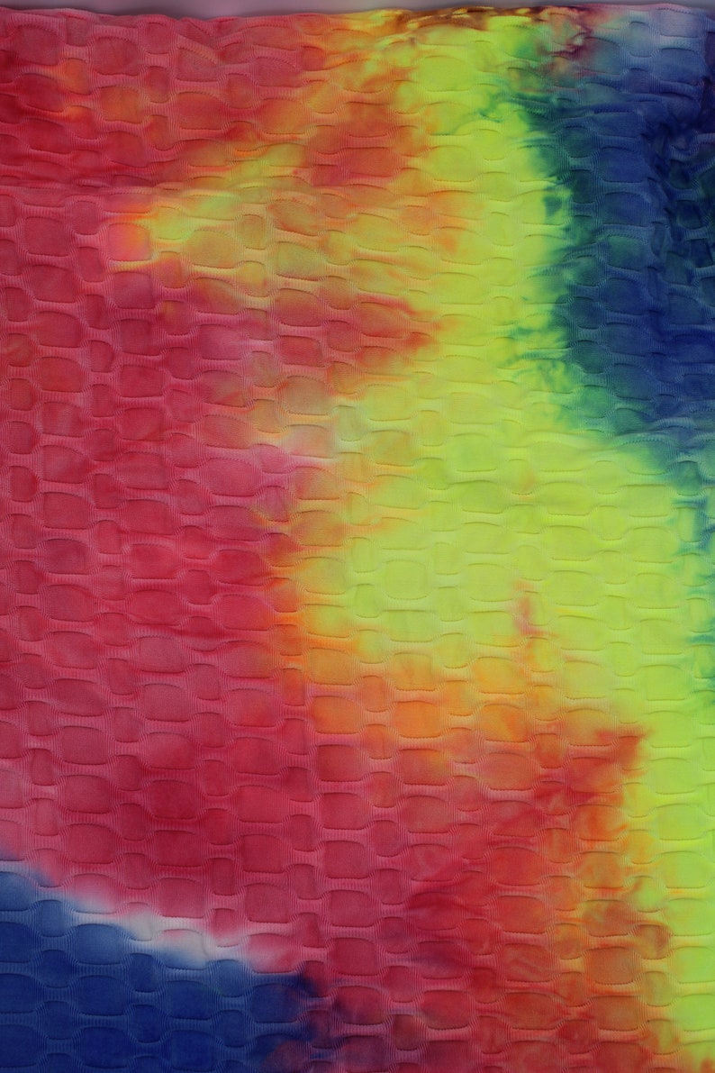May include: A close-up of a tie-dye fabric with a textured, quilted pattern. The fabric is a mix of red, orange, yellow, green, and blue.