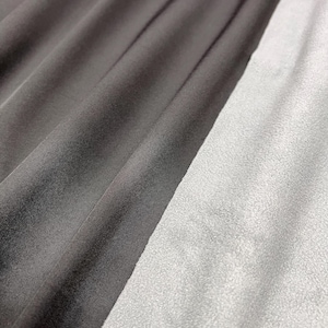 May include: Close-up of two fabric swatches, one black and one white. The black fabric is smooth and silky, while the white fabric is fuzzy and textured.