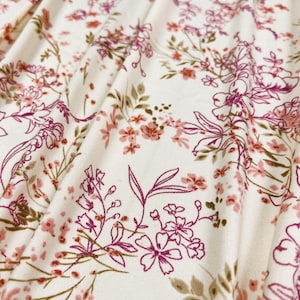 Puede incluir: Tela blanca con estampado floral rosa y marrón. La tela tiene una textura suave y fluida.