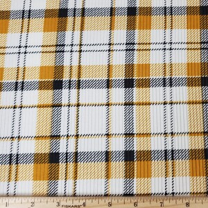May include: White fabric with a yellow and black plaid pattern. The fabric has a ribbed texture. A ruler is included in the image for scale.