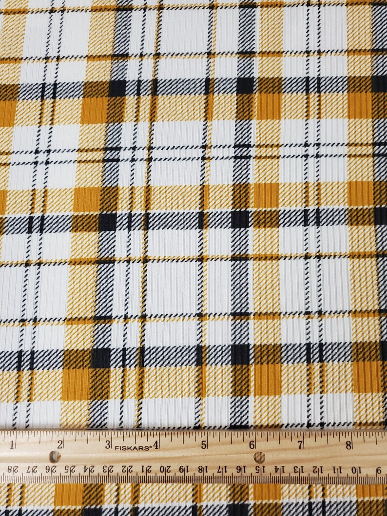 May include: White fabric with a yellow and black plaid pattern. The fabric has a ribbed texture. A ruler is included in the image for scale.