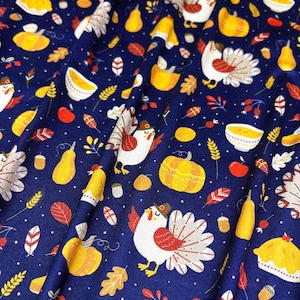 May include: A navy blue fabric with a repeating pattern of turkeys, pumpkins, pears, leaves, and bowls of soup. The turkeys are wearing pilgrim hats and have red and white feathers. The pumpkins are orange and yellow. The pears are yellow. The leaves are orange, yellow, and brown. The bowls of soup are white with a yellow rim.