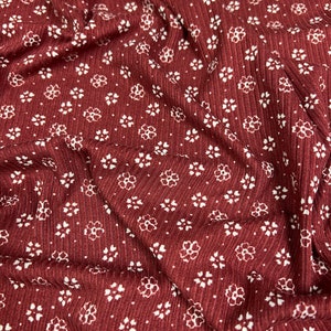May include: Red fabric with a white floral pattern. The fabric has a ribbed texture.