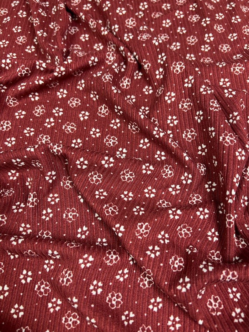 May include: Red fabric with a white floral pattern. The fabric has a ribbed texture.