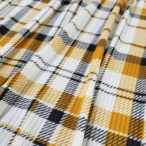 May include: White fabric with a yellow and black plaid pattern. The fabric has a ribbed texture.