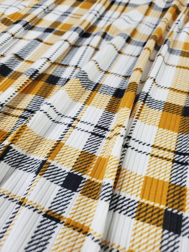 May include: White fabric with a yellow and black plaid pattern. The fabric has a ribbed texture.