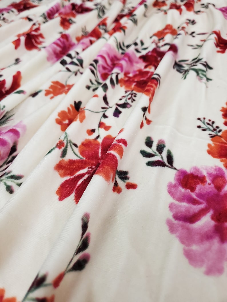 May include: White fabric with a floral print featuring pink, red, and orange flowers. The fabric has a soft, velvety texture.