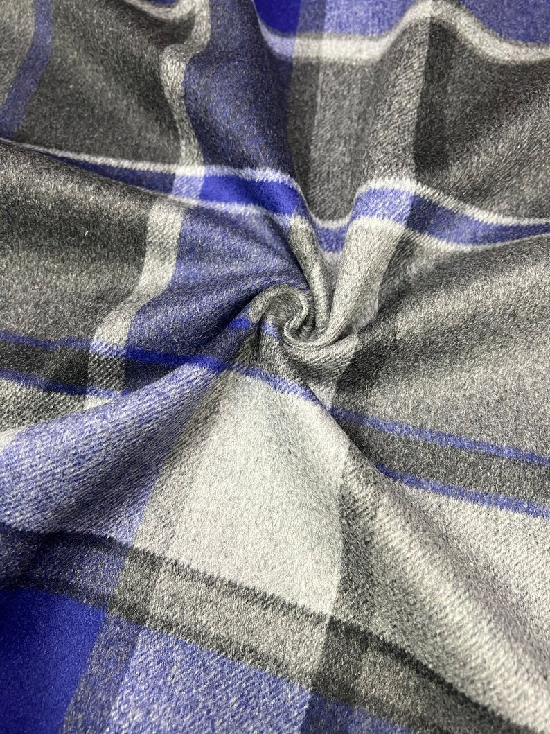 May include: Blue, gray, and white plaid fabric with a soft, textured feel. The fabric is folded and draped, showing the pattern and texture.