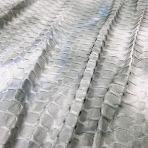May include: Close-up of a grey and blue textured fabric with a subtle tie-dye pattern. The fabric has a raised, textured surface that resembles a honeycomb or waffle pattern.