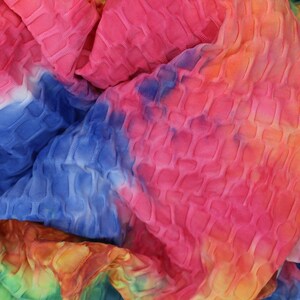 May include: Close-up of a colorful tie-dye fabric with a textured, quilted pattern. The fabric is a mix of pink, blue, yellow, orange, and green.