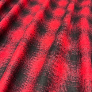 K&ouml;nnte beinhalten: Roter und schwarzer karierter Flanellstoff mit weicher, flauschiger Textur. Der Stoff ist gefaltet und drapiert, wodurch Muster und Textur sichtbar werden.