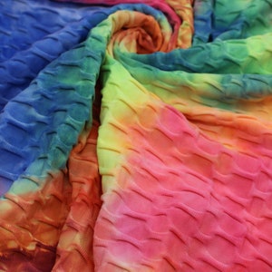 May include: Close-up of a colorful tie-dye fabric with a textured, quilted pattern. The fabric is a mix of pink, orange, yellow, green, and blue.